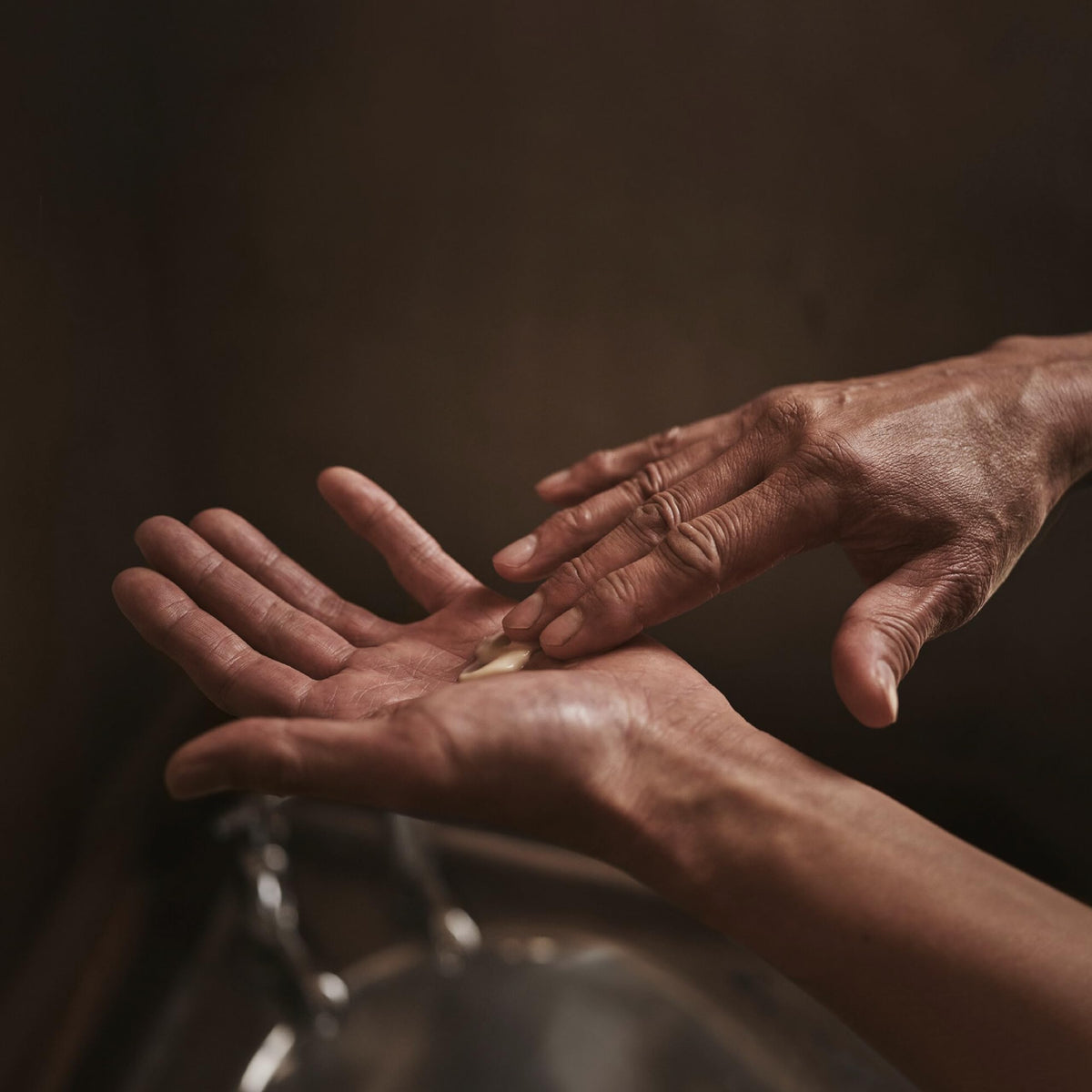 Hand applying balm to elbow, demonstrates Aesop targeted relief for dry areas