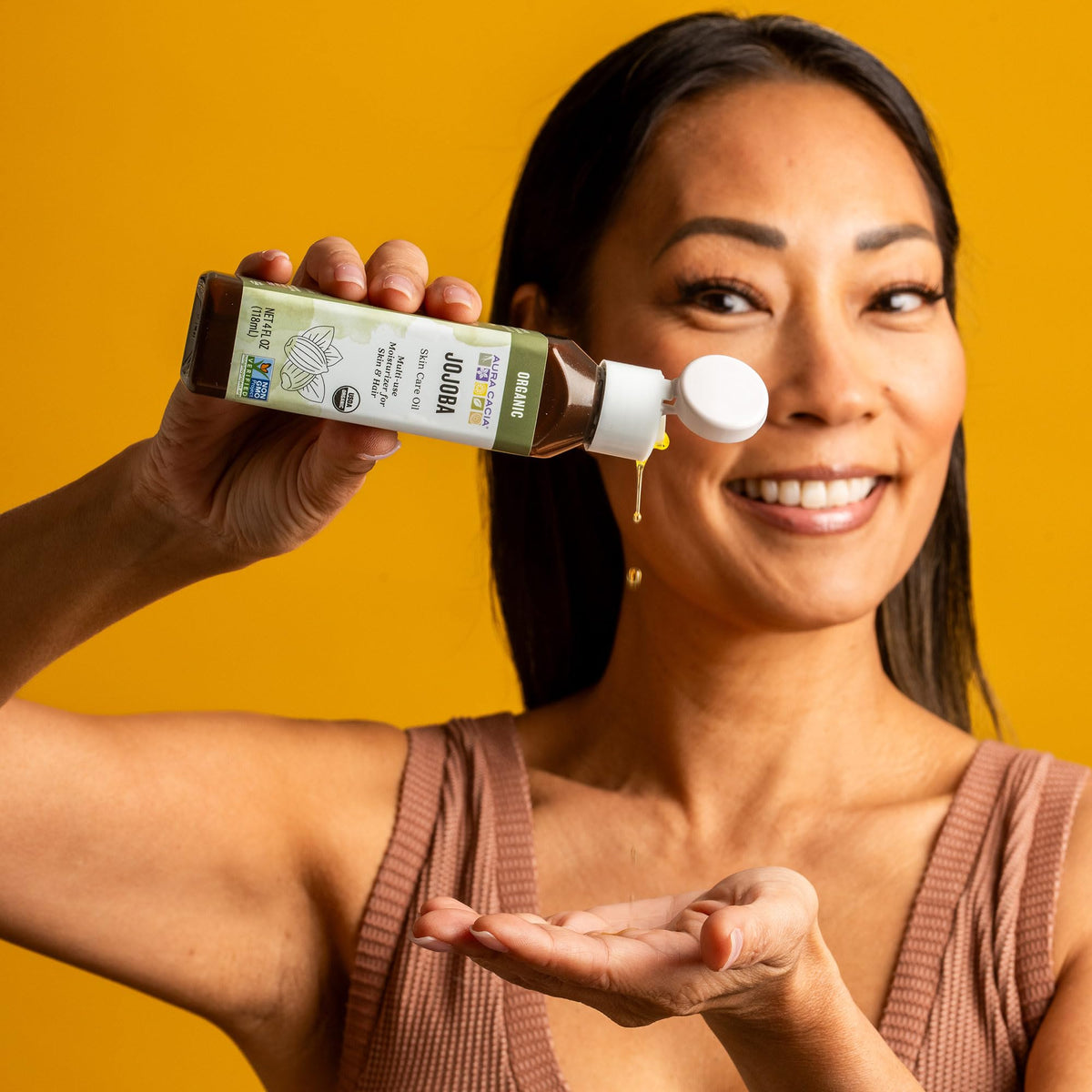 Aura Cacia bottle beside jojoba seeds illustrating botanical sourcing benefit