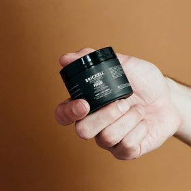 Brickell clay pomade in hands applying to hair showing easy warming and even spread