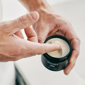 Brickell clay pomade next to ruler showing 2 oz size and travel-friendly convenience