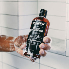 Brickell conditioner in hand under shower indicating easy application and rinse