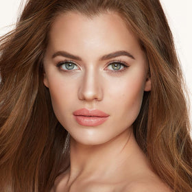 Charlotte Tilbury brush applying highlight to cheek demonstrating natural luminous finish