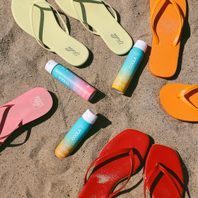 COOLA bottle beside towel in lifestyle shot showing easy packable protection benefit
