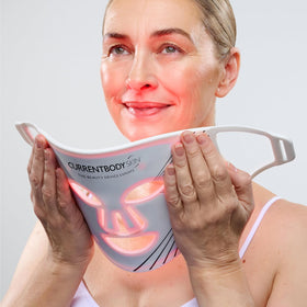 CurrentBody worn by person in living room showing hands-free at-home treatment benefit