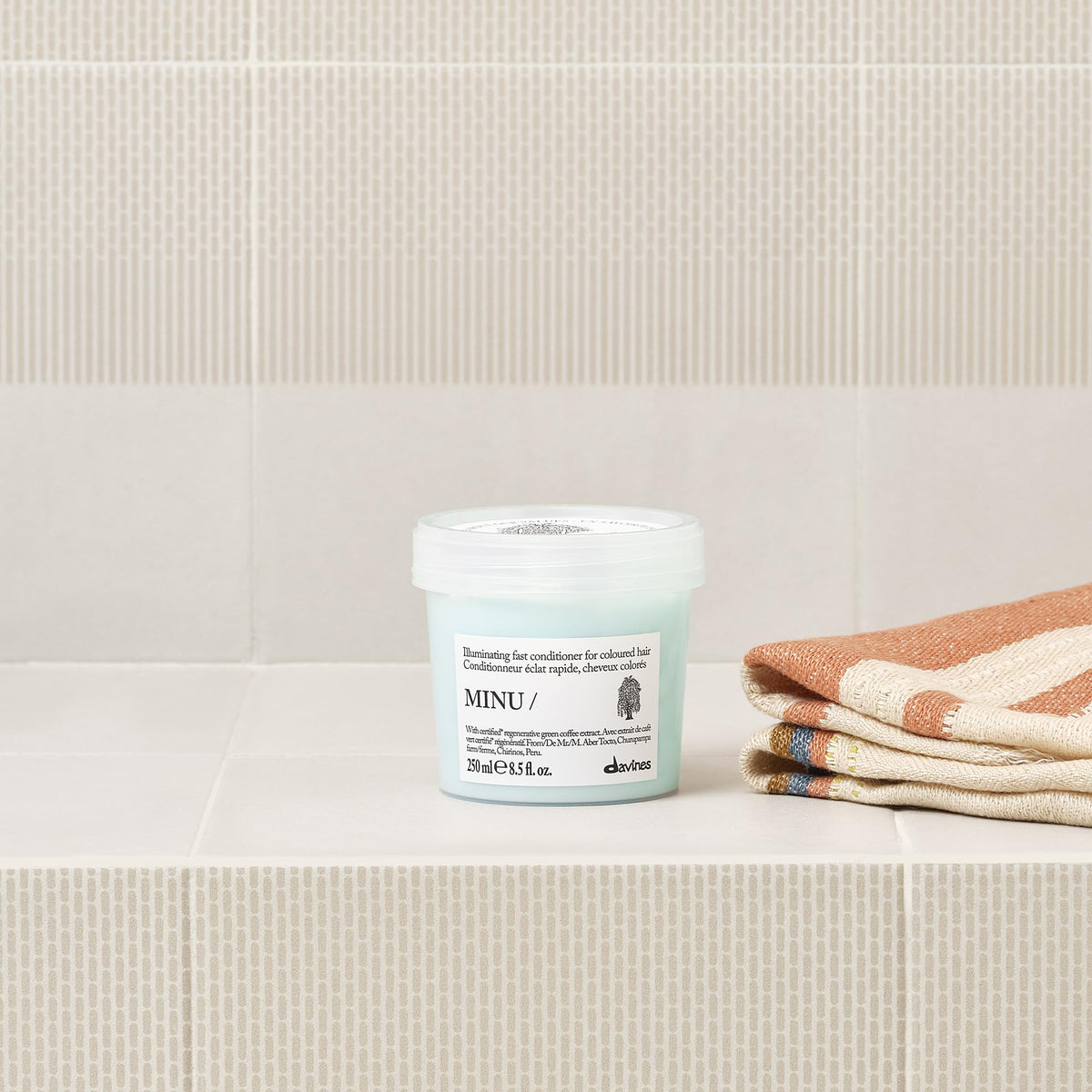 Davines MINU 8.5 oz bottle held in hand shows product scale and portability