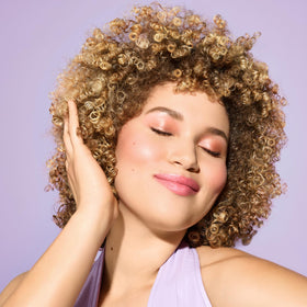 Hands applying DevaCurl cleanser into wet curls showing low-lather coverage