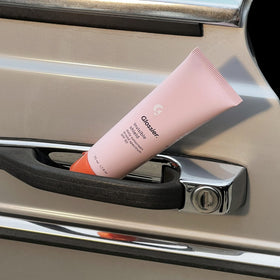 Glossier Invisible Shield staged with beach essentials for daily sun protection