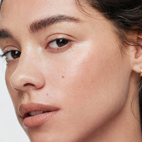 ILIA swiped on skin close-up showing champagne-pearl glow and natural radiance