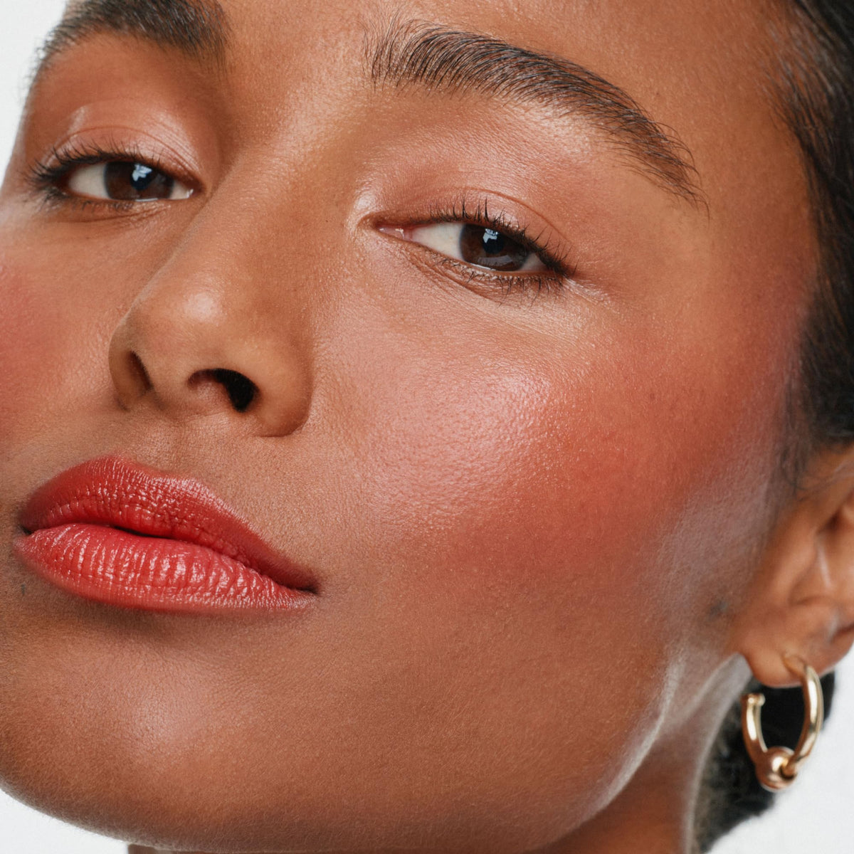 ILIA multi‑stick being applied to cheek by hand for quick natural blush