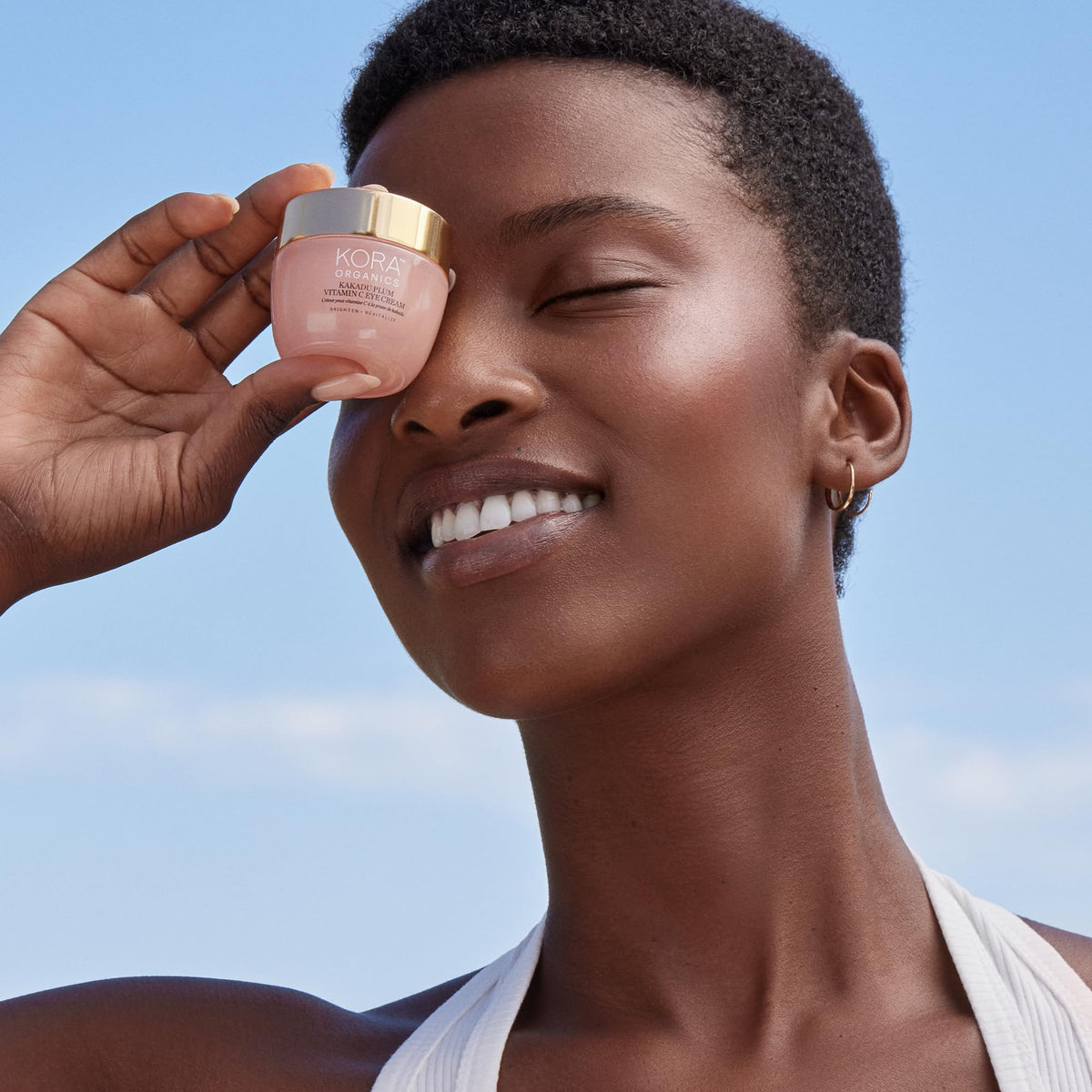 KORA Organics eye cream held in hand showing compact travel-friendly size