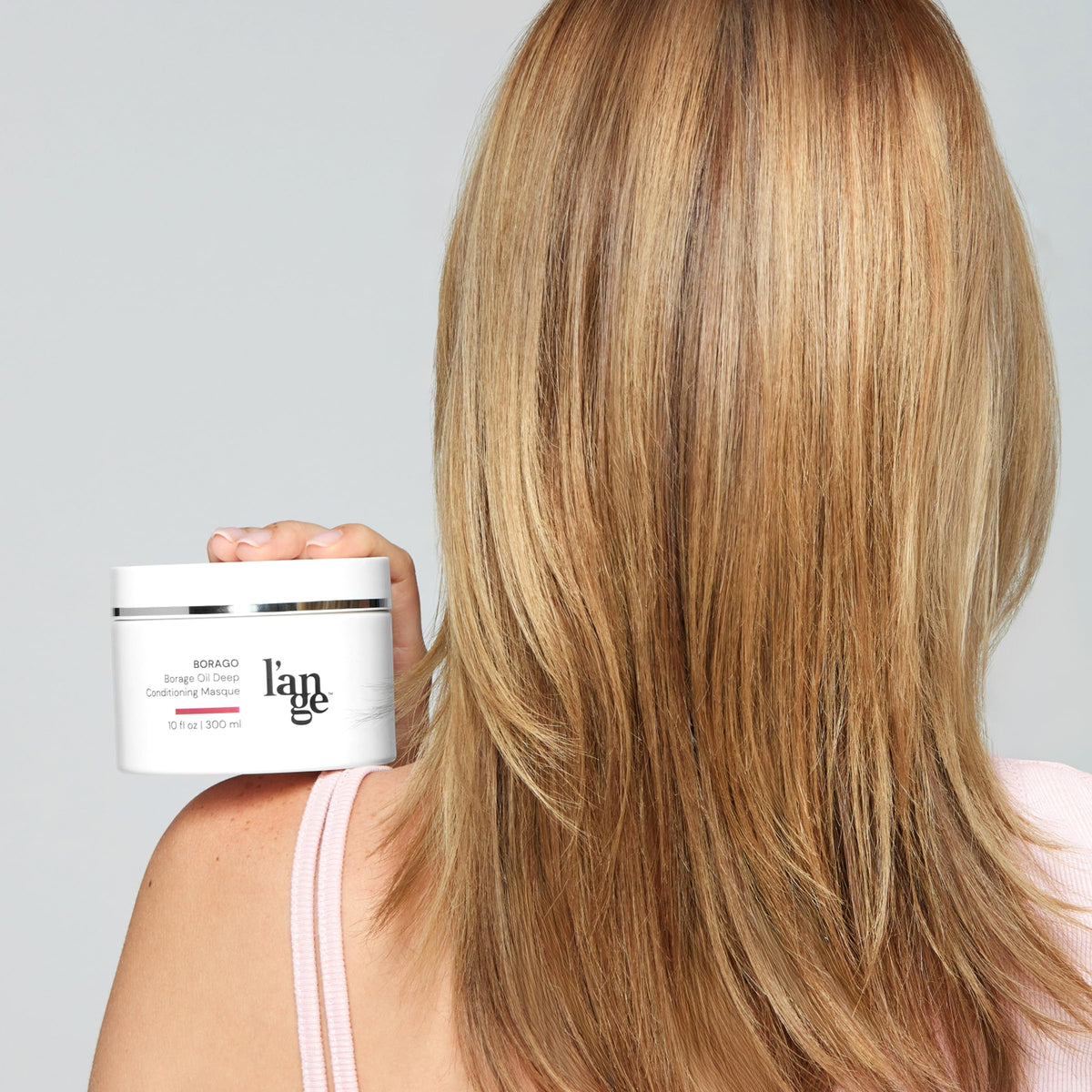 L'ANGE HAIR jar in hand showing 10 oz size for accurate scale
