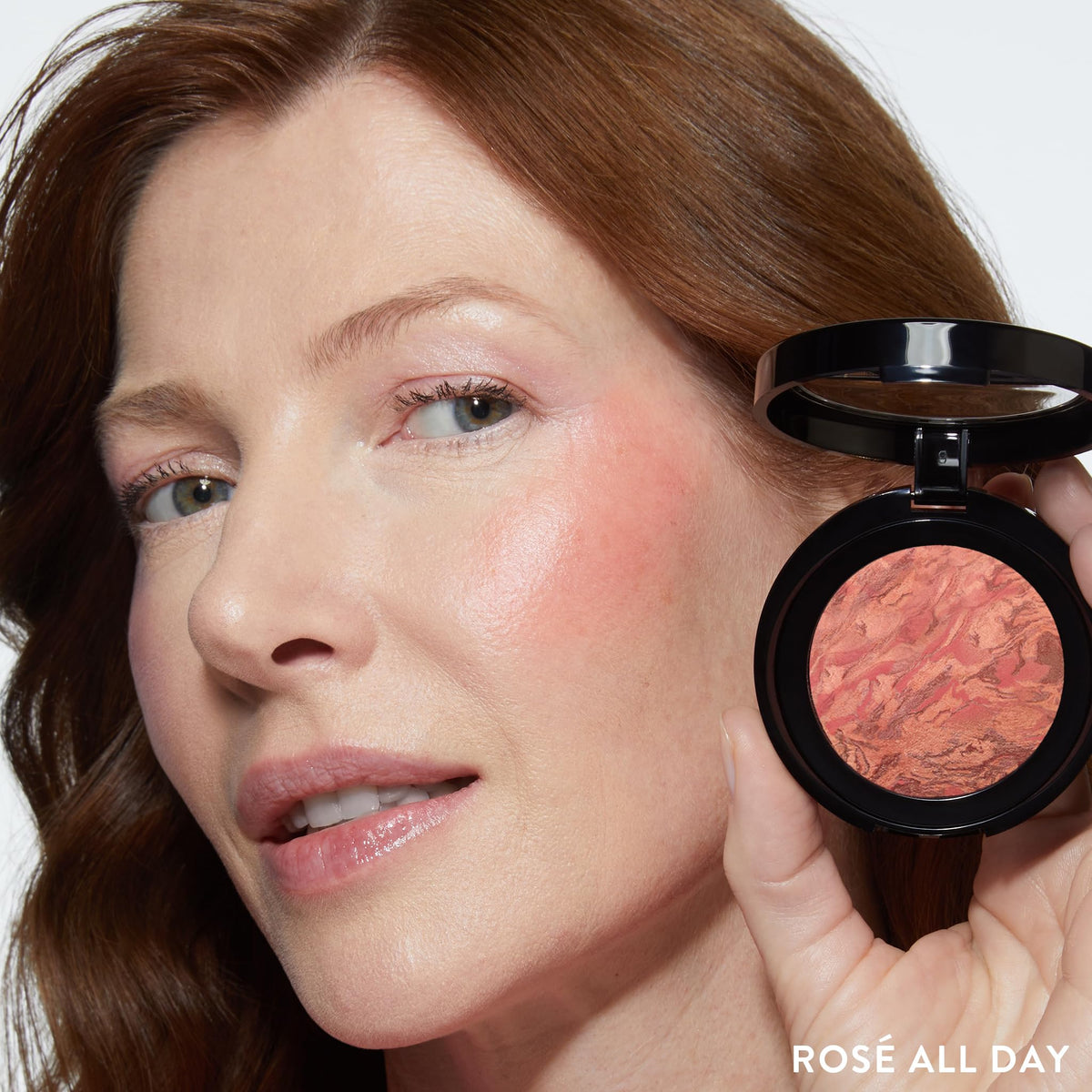 LAURA GELLER NEW YORK brush applying blush to cheek demonstrating lift and natural flush