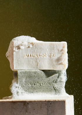 MALIN+GOETZ bar on shower shelf in tiled setting, suggesting daily ritual and warm scent
