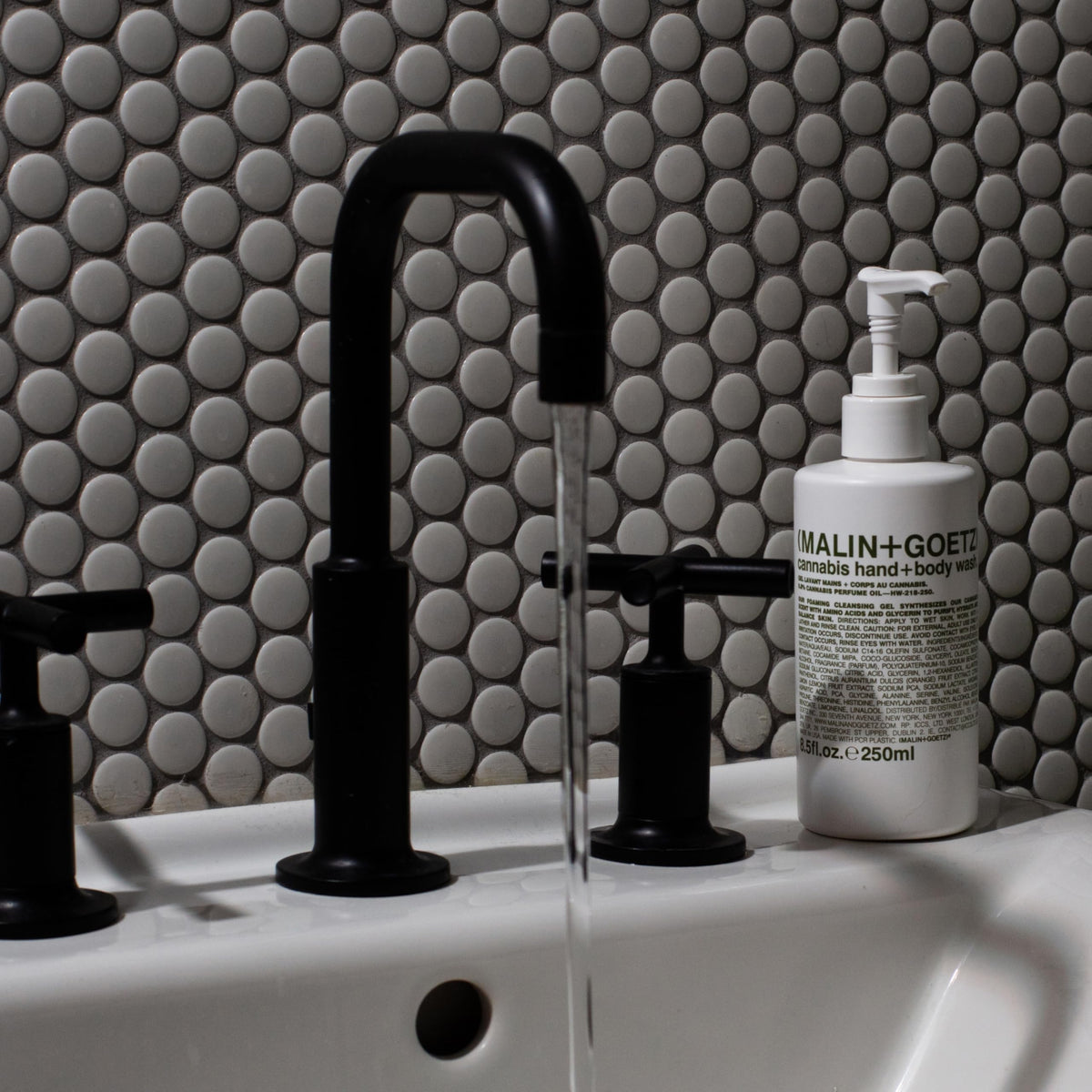 MALIN+GOETZ bottle on shower shelf lifestyle scene suggesting daily ritual relaxation benefit