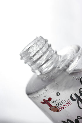 MINI MANI MOO bottle beside a hand for scale showing travel-friendly 10 mL size