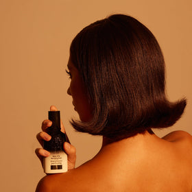 Oribe Balm D'Or on bathroom counter with styling tools suggesting salon results
