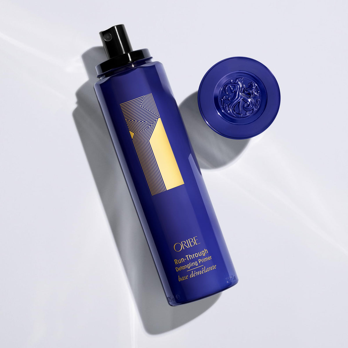 Oribe Run-Through next to common objects to show 5.9oz size and travel-friendly proportions