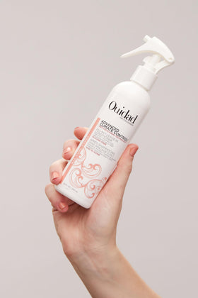 Bottle beside hand for scale showing Ouidad travel-friendly 8.5 fl oz size