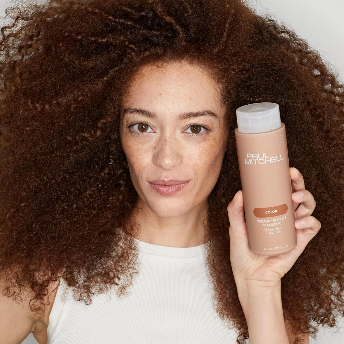 Paul Mitchell 33.8 fl oz bottle next to a hand for size comparison and long‑use benefit
