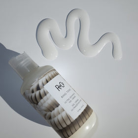 R+Co Ring Tone on a bathroom counter with greenery, suggesting daily styling ritual