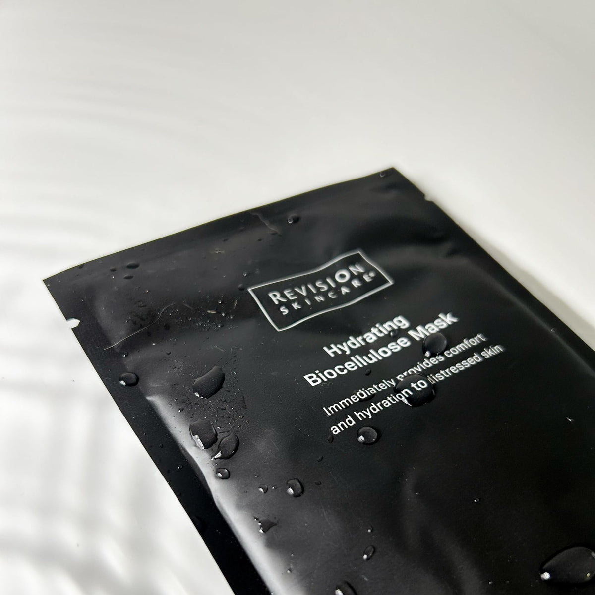 Revision Skincare serum droplet on edge of sheet highlighting concentrated hydrating essence
