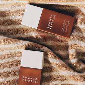 Summer Fridays bronzing drops on bathroom shelf with plants, evokes routine simplicity and radiance
